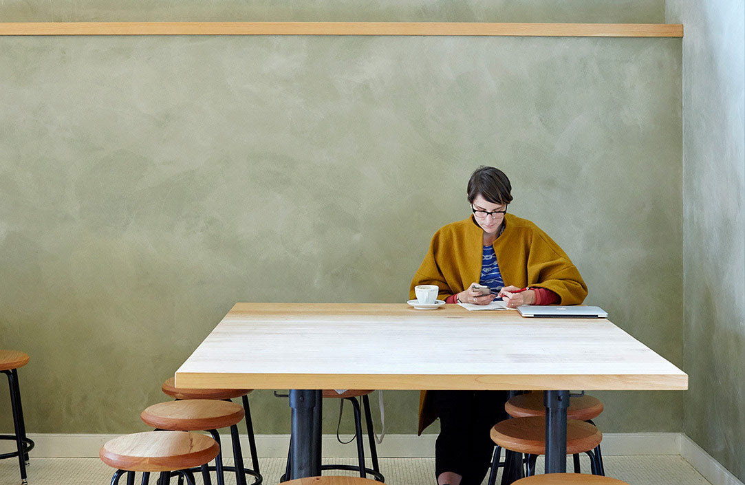 A guest sitting at a table at Sightglass Coffee's Divisadero (San Francisco) location. The pale green wall and the contrast with the guest clothes gives a Hopper vibe to the scene.